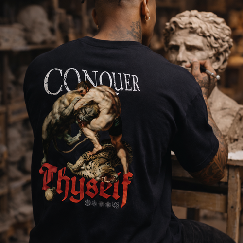 Person wearing a black t-shirt with 'Conquer Thyself' design in a workshop setting.