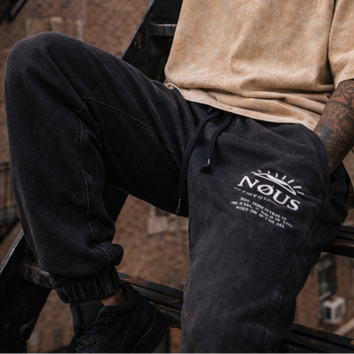 Man sitting on a fire escape wearing a beige t-shirt and black pants with text.