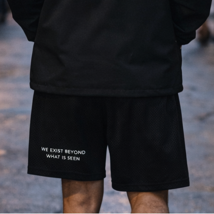 Person wearing a black hoodie with a white logo walking on a street at night.
