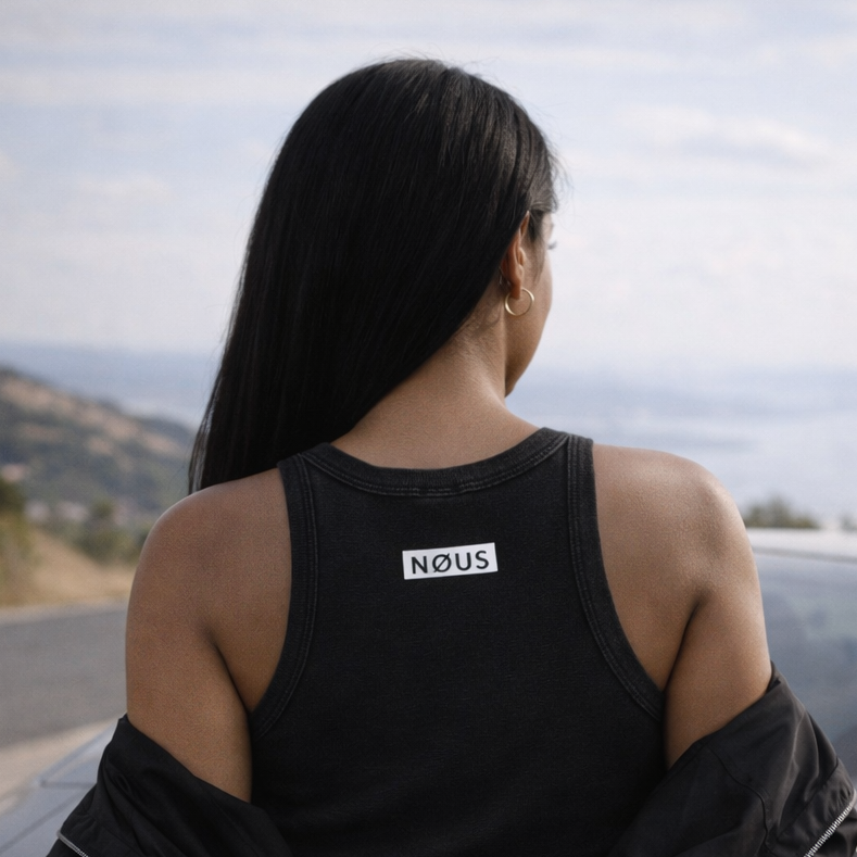 Person wearing a black outfit with 'NOUS' branding, standing next to a car.
