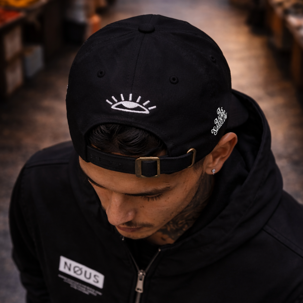 Person wearing a black cap and jacket with 'NOUS' branding in an indoor setting.