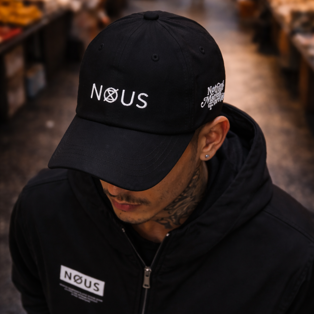 Person wearing a black cap and jacket with 'NOUS' branding in an indoor setting.