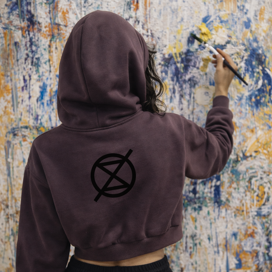 Person wearing a hoodie with a symbol, painting on a textured wall.