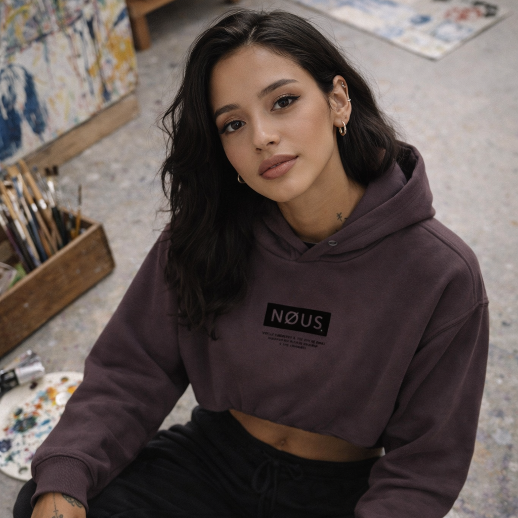 Woman wearing a purple hoodie with 'NOUS' logo, sitting on the floor in an artistic setting.