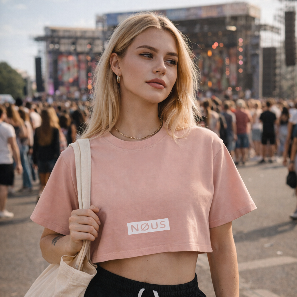 Woman wearing a pink 'NOUS' crop top and black shorts at a music festival.