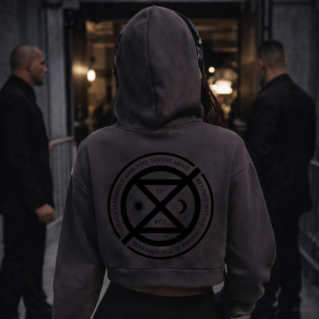 Person wearing a hoodie with a logo on the back, standing in a dimly lit area with other people.